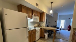 Una cocina con armarios de madera, un refrigerador blanco, un microondas, una estufa y un cesto de basura.