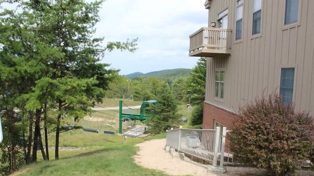 Un bâtiment doté d’un balcon, un chemin menant à une aire de jeux et un espace verdoyant avec des arbres.