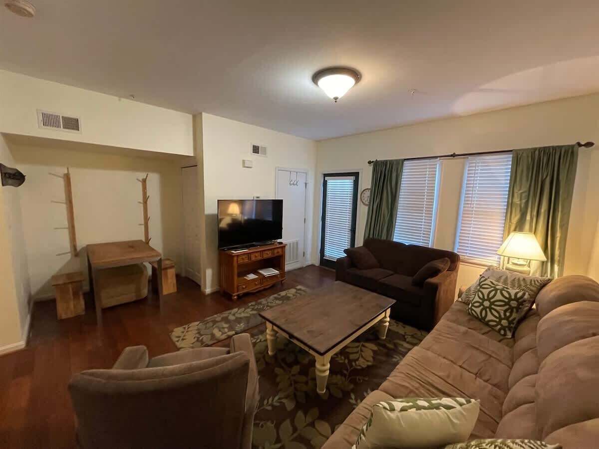 A living room with a sofa, armchair, coffee table, TV stand, and a small table with a lamp.