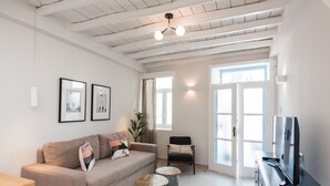 Uma sala de estar com sofá, dois banquinhos redondos, uma poltrona, televisão e quadros nas paredes.