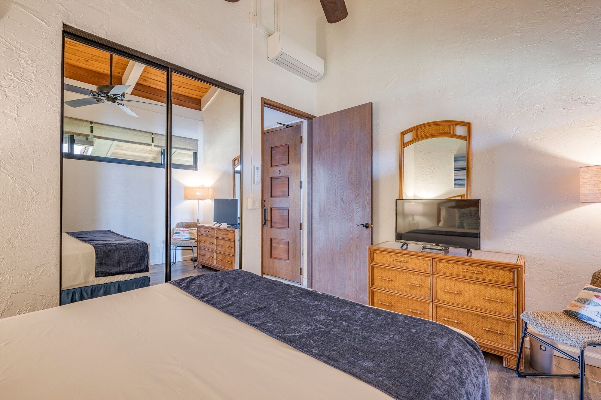 A bedroom with a bed, a dresser, a mirror, and a ceiling fan.