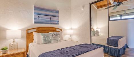A bedroom with a large bed, two bedside tables with lamps, a mirror, and a ceiling fan.