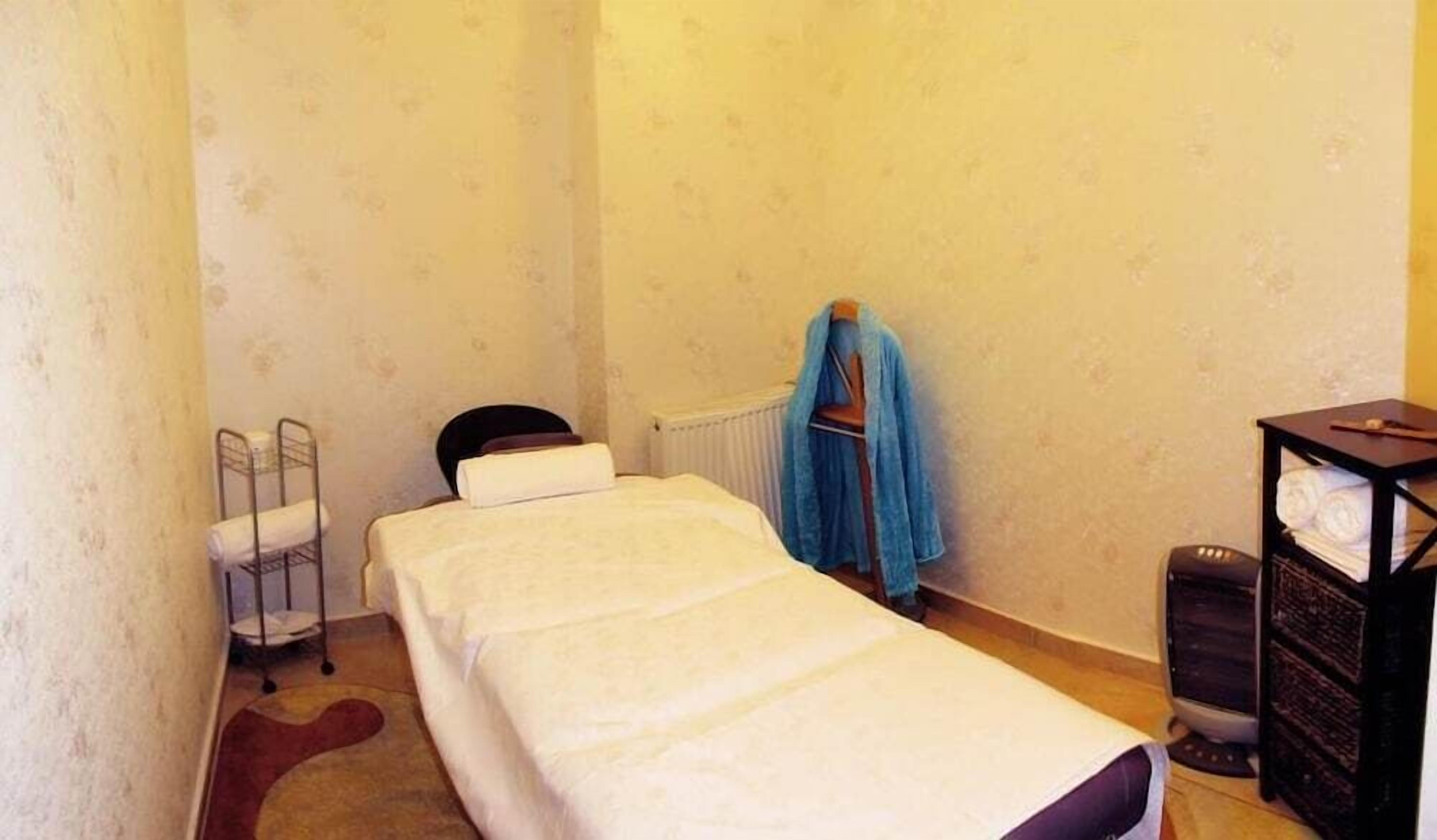 A small, single-bed room with a radiator, a small table with a lamp, and a blue towel hanging on the wall.