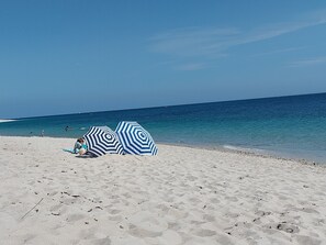 A beach with two striped umbrellas and a person sitting on the sand. - Jolie Maison Rénovée, à 2 min en Voiture des Plages et du Port du Guilvinec (Treffiagat)