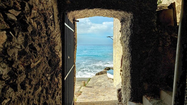 Un arco de piedra que da a vistas costeras con una embarcación en la orilla.