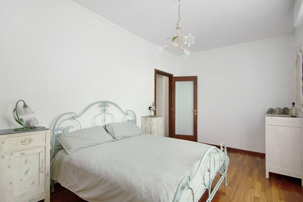 Un dormitorio con cama, mesitas de noche, cómoda, puerta y una araña.