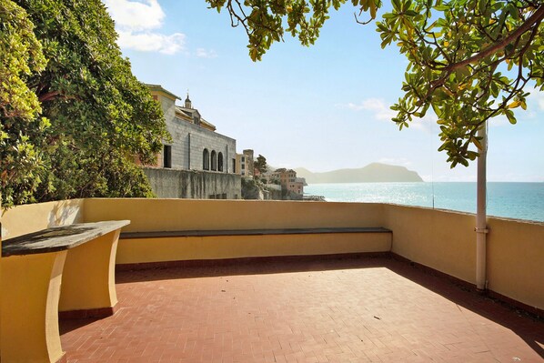 A terrace with a view of the sea and a building in the background.