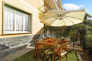 Un patio al aire libre con una mesa y sillas de madera, un paraguas grande y una ventana con cortinas.