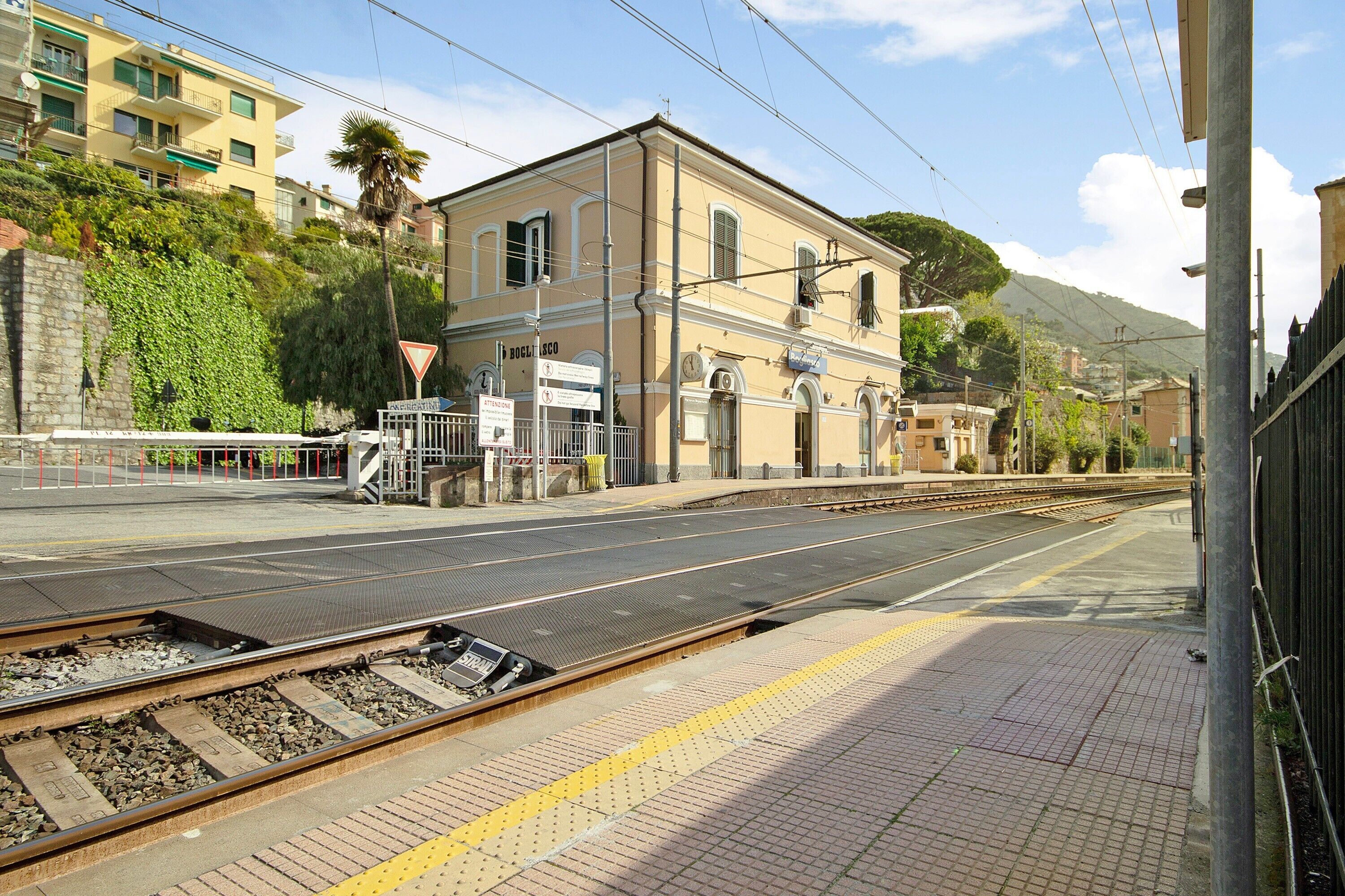 Eine Bahnsteig mit einem Gebäude im Hintergrund, einer Fußgängerüberweg und einem Gleis.