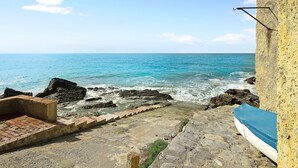 Vista costera con una escalera de piedra que baja a una playa, un bote y un cielo despejado.