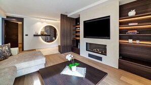 Un salon moderne comprenant un canapé, une table basse avec une plante, une cheminée, un téléviseur fixé au mur et des étagères intégrées.