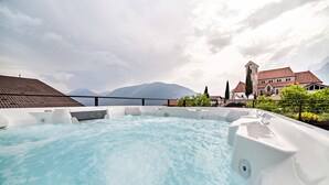 Un bain à remous avec une vue sur les montagnes, une église et un bâtiment avec un toit rouge.
