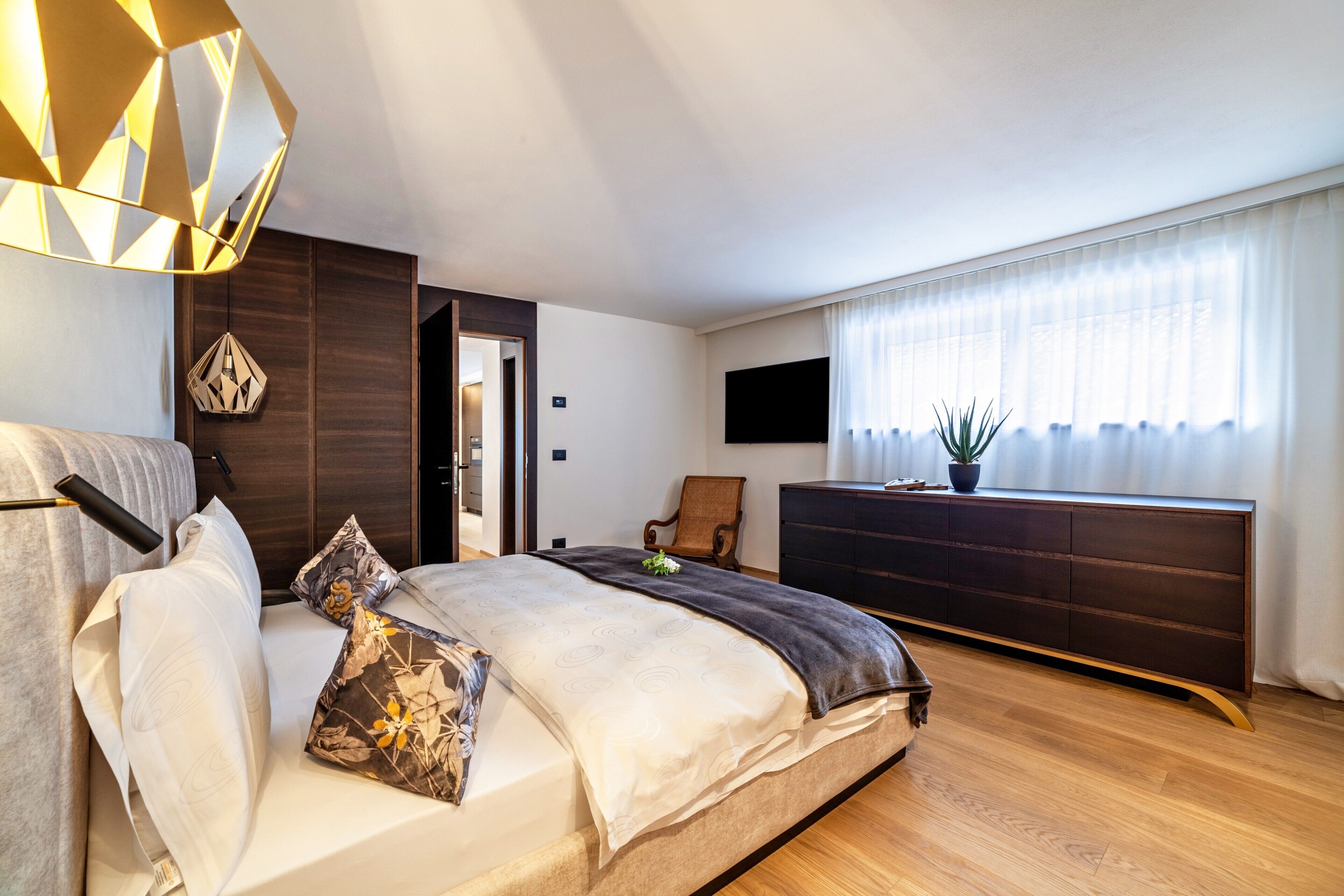 A modern bedroom with a bed, bedside table, TV, and a large window with curtains.