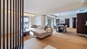 Un salon moderne avec un canapé d’angle, une table à manger avec des chaises et, au fond, un coin cuisine.