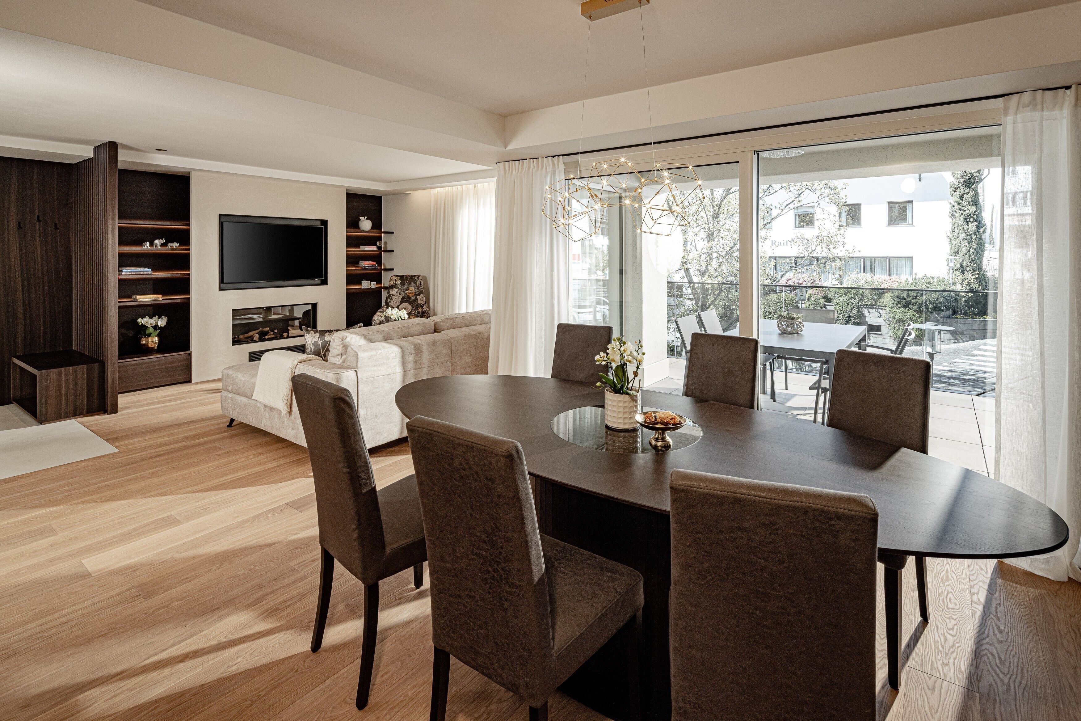 Un salon moderne comprenant un coin repas, un téléviseur à écran plat fixé au mur et une grande fenêtre donnant sur l’extérieur.