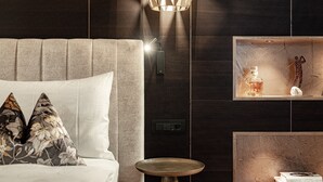 Une chambre moderne avec une tête de lit capitonnée, une table de chevet, un luminaire fixé au mur et une étagère ornée d’objets décoratifs.