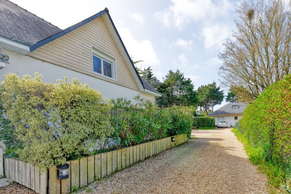 A house with a gravel driveway, wooden fence, and a garden with various plants.