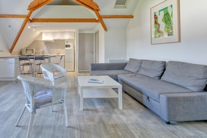 A modern loft-style living space with a dining area, a gray sofa, wicker chairs, and a white coffee table.