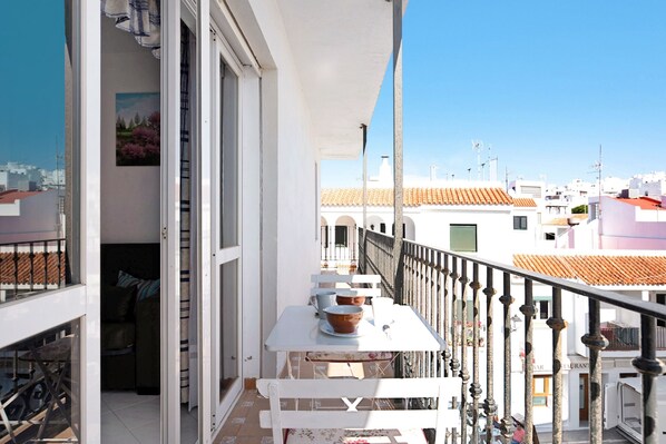 A balcony with a table and chairs, a view of buildings, and a railing.