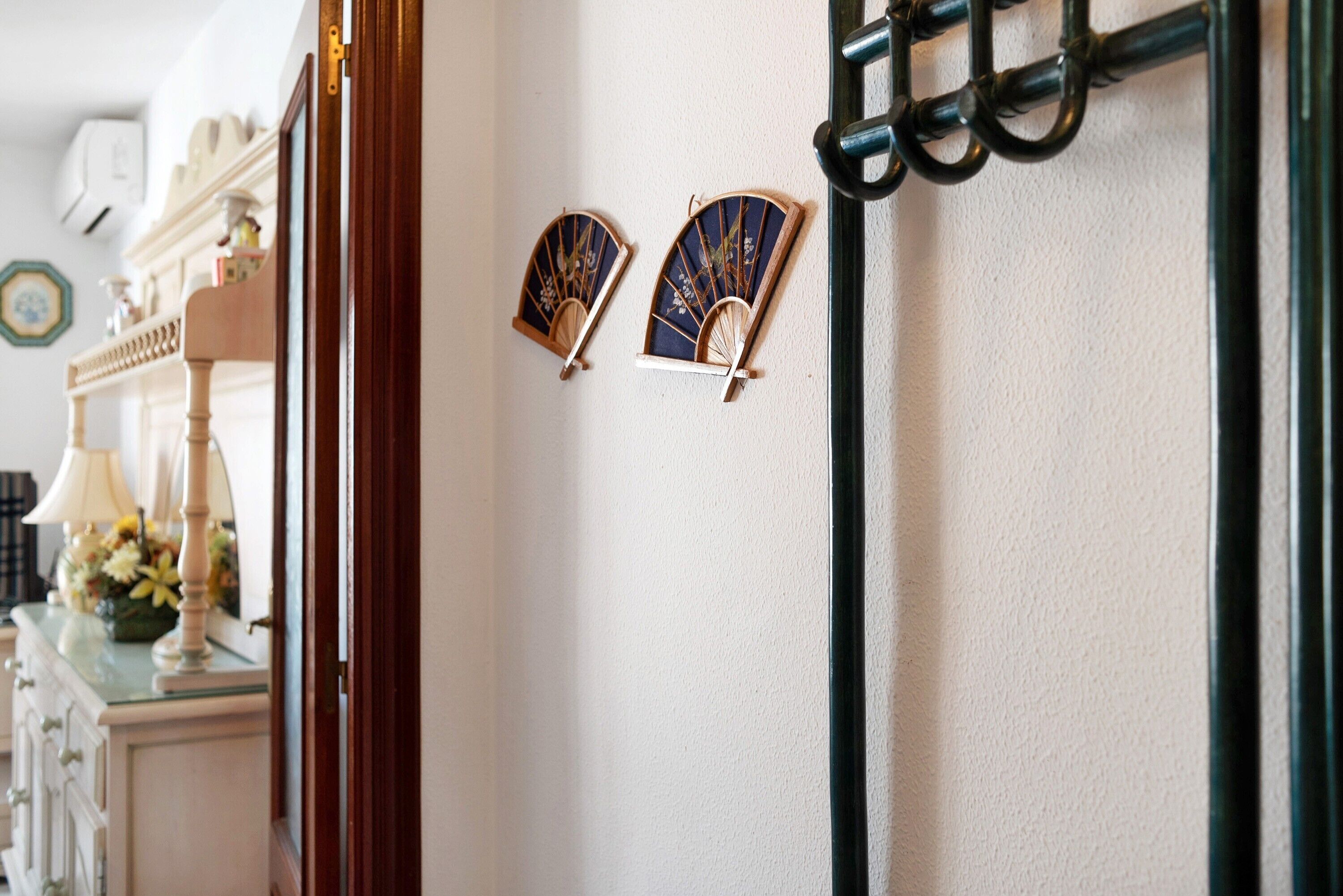 Een kamer met een witte muur, een houten deur en een zwarte metalen kapstok met twee ventilatoren.