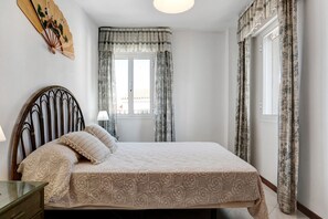 A bedroom with a bed, a bedside table, a wall-mounted fan, and a window with curtains.