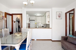 A dining area with a glass table, chairs, and a kitchen in the background.