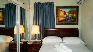Habitación de hotel con cama, dos mesitas de noche, lámpara, un cuadro y ventana con cortinas.