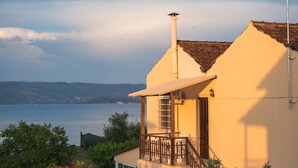 A house with a balcony overlooking a body of water and hills in the distance. - Saint Peter Bay – 1st Floor Holiday Home with Shared Pool, Wi-Fi & Air Conditioning (Lefkimmi)