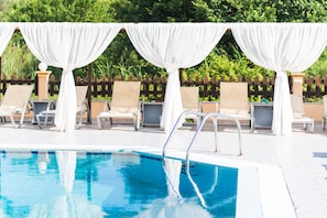 A pool area with white drapes, lounge chairs, and a clear blue pool.