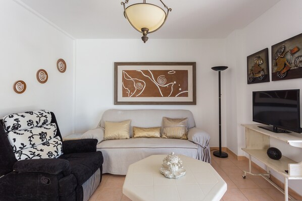 A living room with a sofa, a coffee table, a TV, and artwork on the wall. - Holiday Home "Carmen" with Sea View, Terraces & Wi-Fi (Oliva)