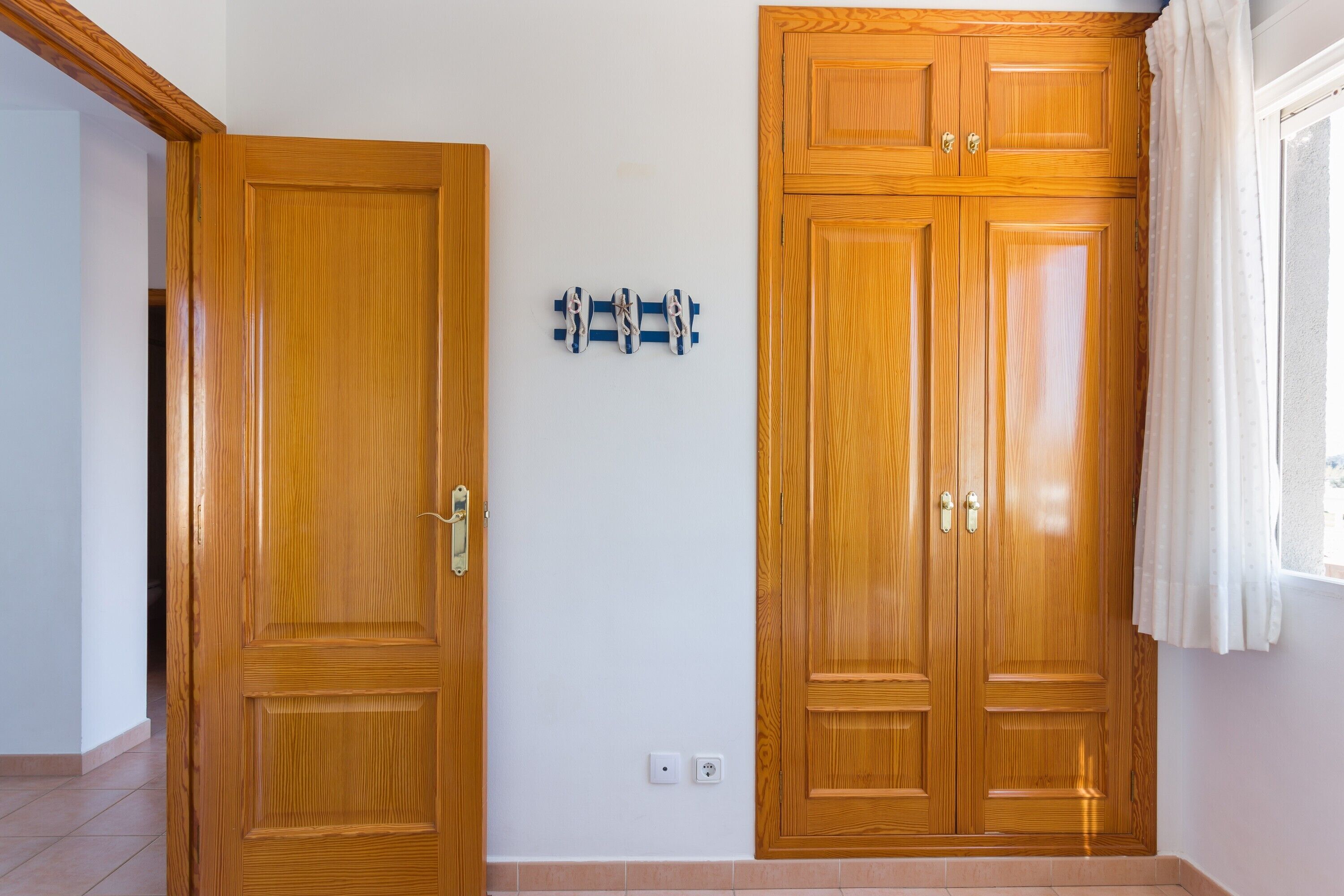 A room with two wooden doors, a wall-mounted shoe rack, and a window with curtains.