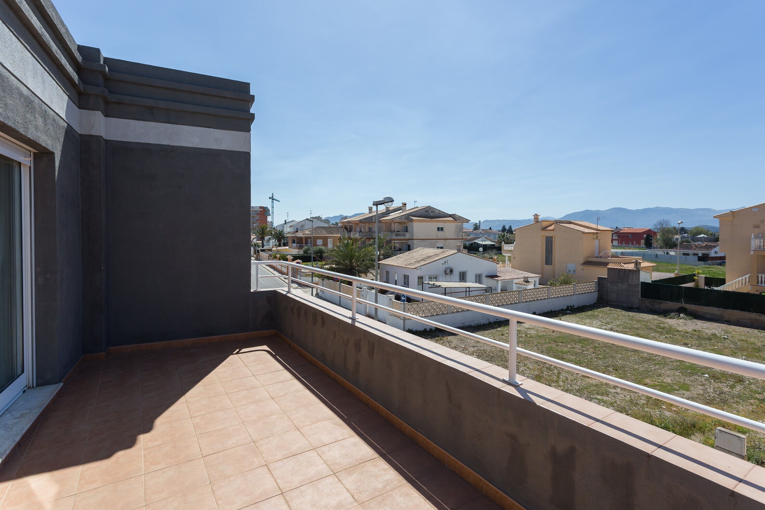 Ein Balkon mit Fliesenboden, Geländer und Blick auf umliegende Gebäude und Berge.