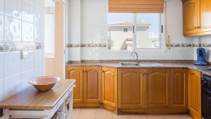 Une cuisine avec des meubles de rangement en bois, une fenêtre avec un store, un évier et une machine à café.