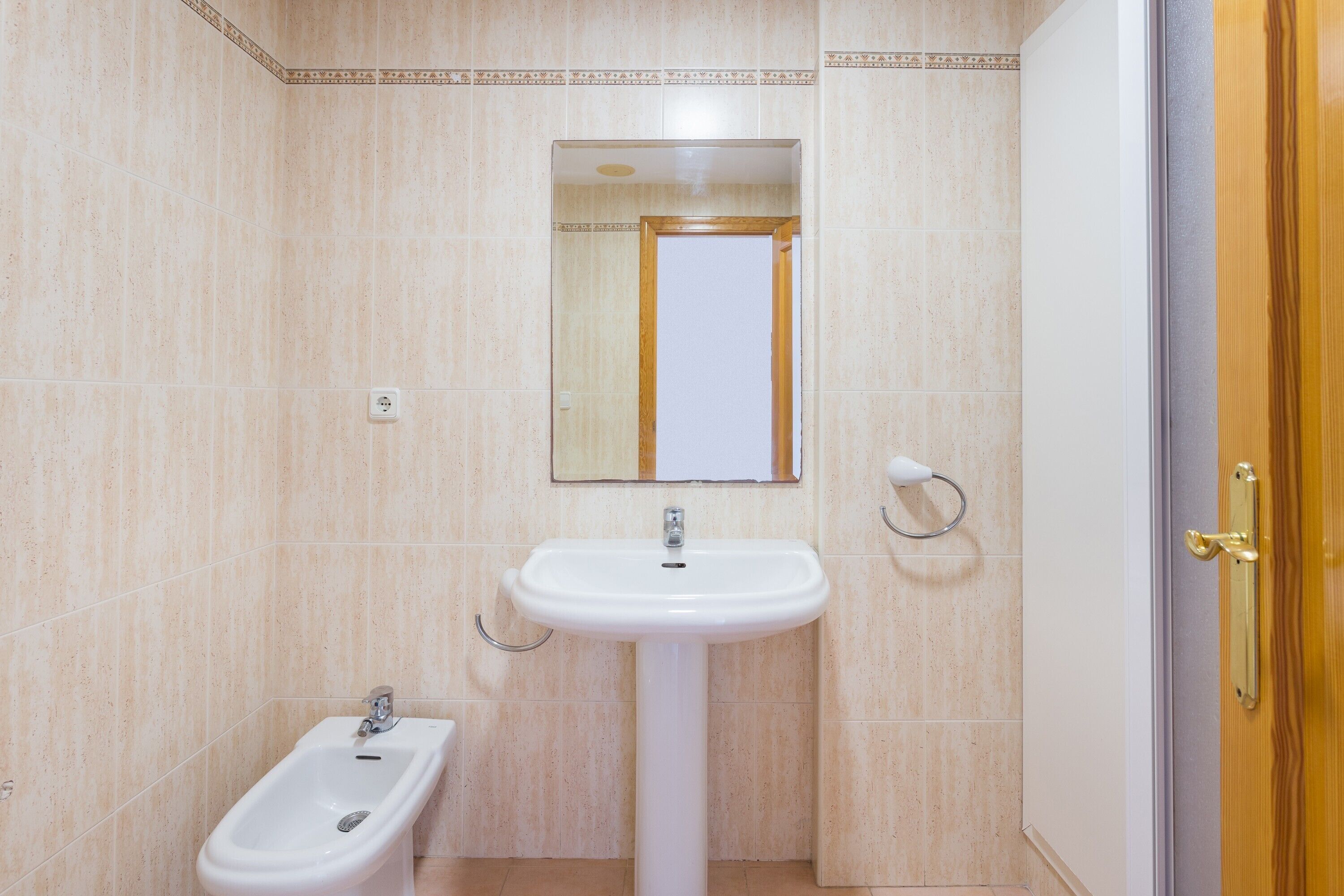 Un bagno con un lavandino su piedistallo, un bidet, uno specchio e una porta con maniglia in ottone.
