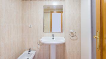 Un bagno con un lavandino su piedistallo, un bidet, uno specchio e una porta con maniglia in ottone.