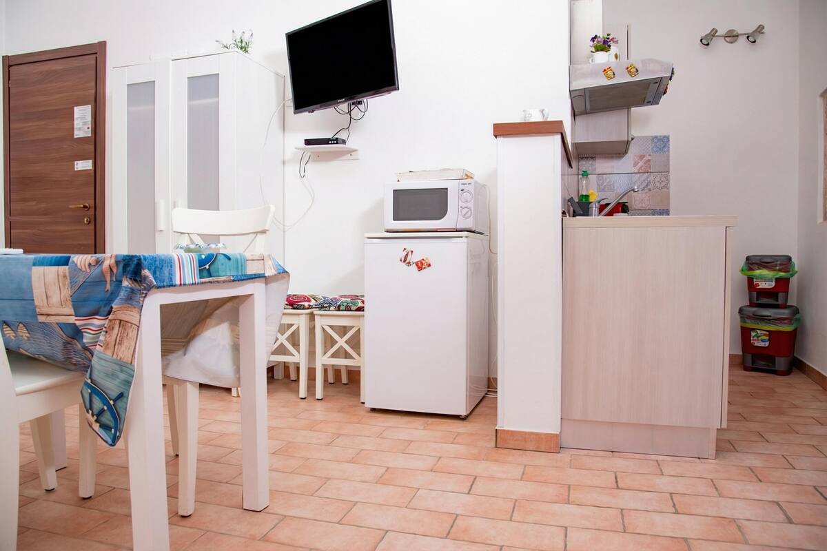 Une cuisine compacte  équipée d’un four à micro-ondes, d’un petit réfrigérateur, d’un meuble en bois et d’un téléviseur fixé au mur.