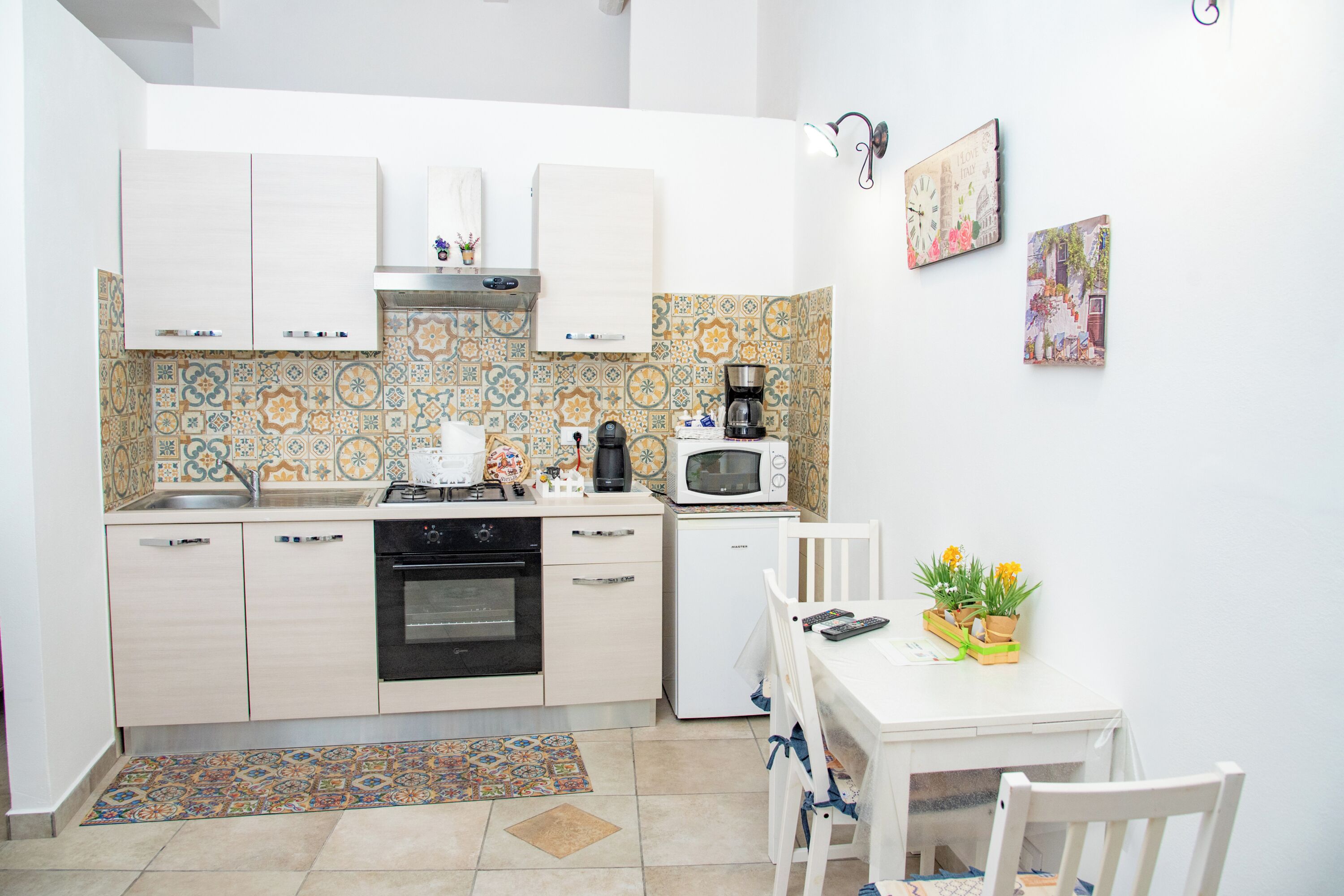 A compact kitchen with white cabinets, a microwave, a coffee maker, and a small refrigerator.