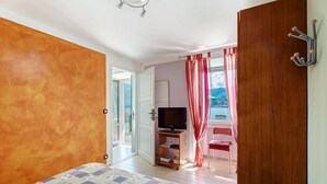 Una camera da letto con un letto, una televisione su un mobile, una sedia rossa e una porta in legno.
