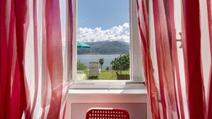 Una stanza con finestra, tende, una sedia e vista su un lago e montagne.