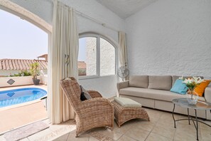 A room with a pool, a wicker chair, a sofa, and a fan.
