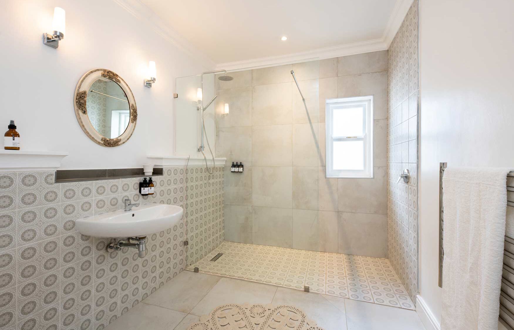 A bathroom with a sink, mirror, shower, and patterned tiles.