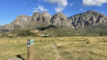 Paisaje montañoso con cielo despejado, un camino de tierra que lleva a un edificio y una señalización al frente.