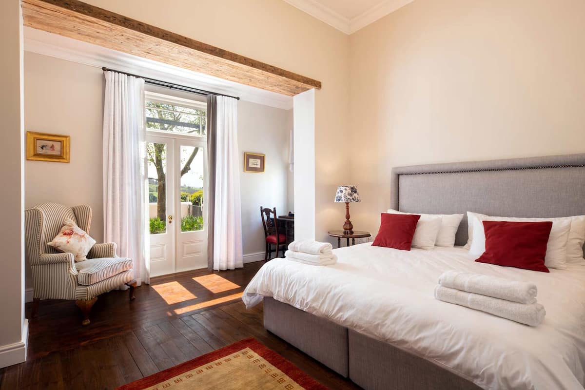 A bedroom with a large bed, a chair, a table with a lamp, and a view through a door.