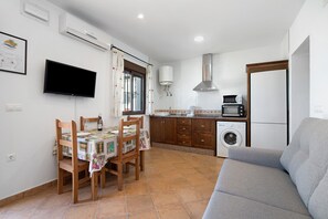 A compact kitchen with a washing machine, a microwave, and a dining area with chairs and a table.