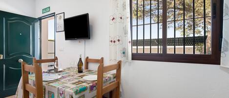 A dining area with a table set for four, a television mounted on the wall, and a window with bars.