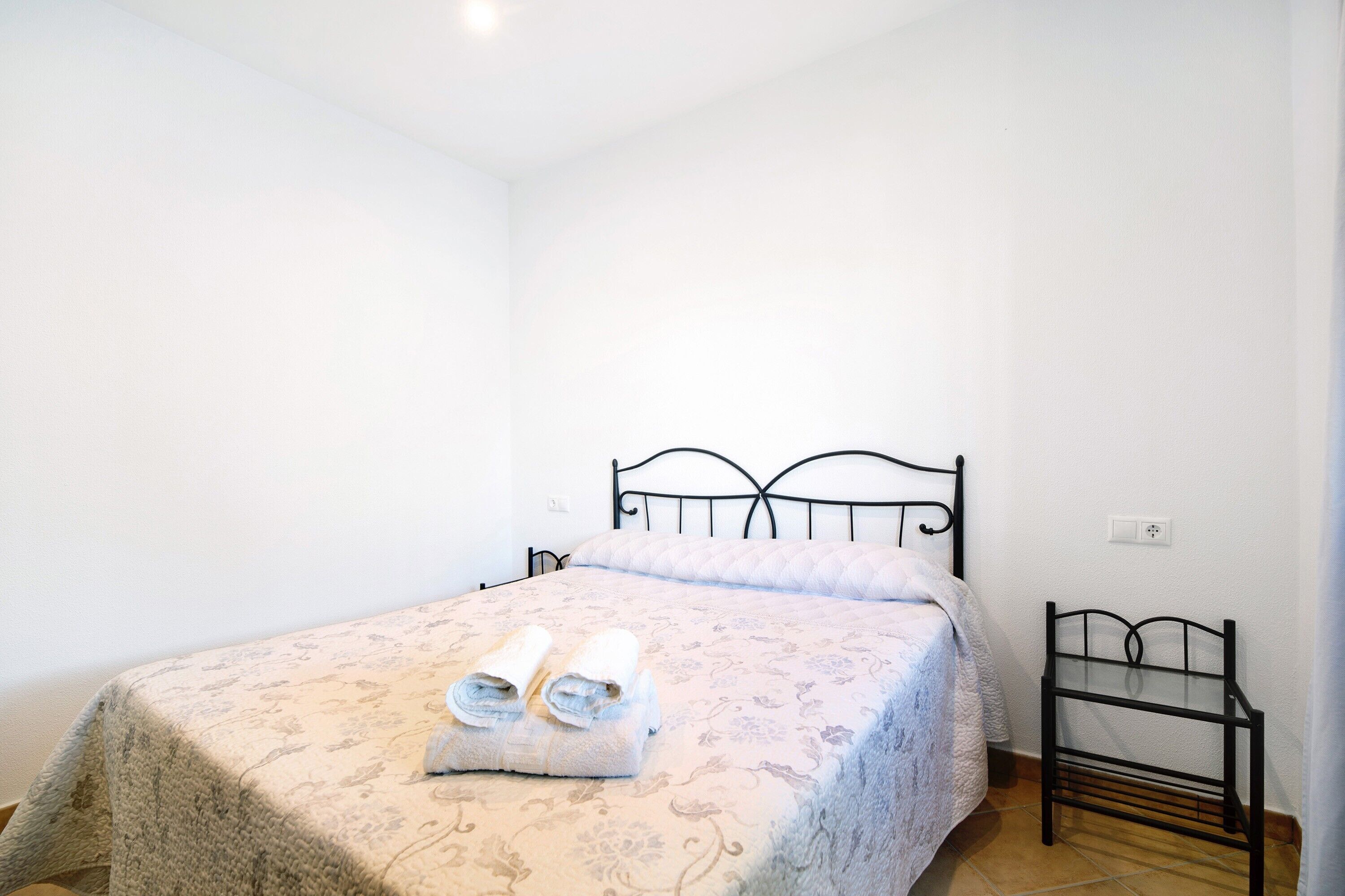 Un dormitorio con cama, mesita de noche y toma de corriente.