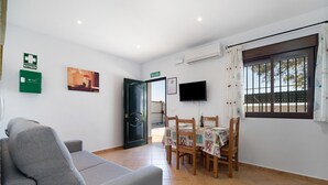 A room with a sofa, a dining table with chairs, a TV, and a door marked 'SALIDA'. - Holiday Home "Novobarrosa A" with Sea View, Shared Pool & Wi-Fi (Chiclana de la Frontera)