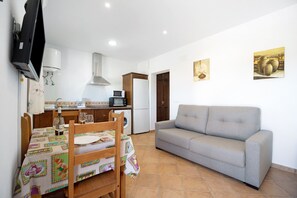 A room with a sofa, a dining table with chairs, a kitchen area, and two paintings on the wall.