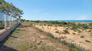 A coastal landscape with a clear sky, a sandy area with sparse vegetation, and a structure with a glass barrier on the left. - Holiday Home "Novobarrosa A" with Sea View, Shared Pool & Wi-Fi (Chiclana de la Frontera)