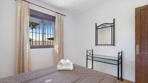 Ein Schlafzimmer mit Bett, Fenster mit Vorhängen, Nachttisch und Tür.